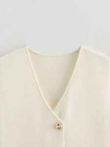 Close-up of knit vest featuring V-neckline and a decorative round gold button