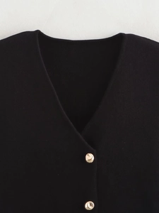 Detail of the V-neck and decorative gold dome buttons on a black knit vest