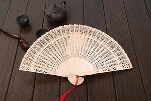 Detailed close-up of a laser-cut sandalwood folding fan with an elegant red silk tassel