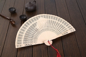Detailed view of hollow carved wooden fan with red tassel on vintage wood background