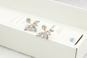 Macro shot of fan-shaped marquise zircon earrings on white box with golden metal base