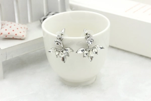 Close-up of silver daisy earrings with marquise cubic zirconia on a white porcelain cup