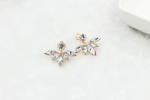 Close-up of gold-finish leaf earrings with marquise-cut zircon on white fur texture