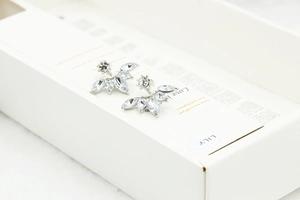 Detail shot of marquise-cut zircon daisy flower earrings with silver studs on a gift box