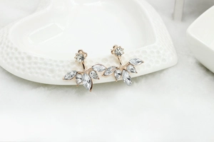Detailed close-up of golden leaf earrings with clear marquise zircon crystals on white porcelain