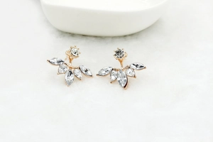 Detail of gold floral stud earrings with white marquise crystals on a white background