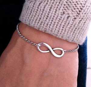 Detail showing a silver infinity symbol bracelet worn on wrist with knitwear background