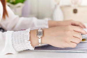 Elegant woman wearing a rose gold rectangular watch with rhinestone details and white band