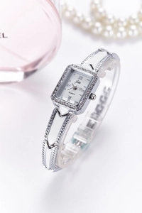 Macro detail of a rectangular silver watch with crystal bezel and a pink perfume backdrop