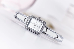 Detailed close-up of a square silver quartz watch with a diamond bezel and bracelet band