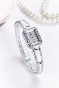 Detail of silver women's quartz watch with rhinestone bezel and elegant pearl accessories