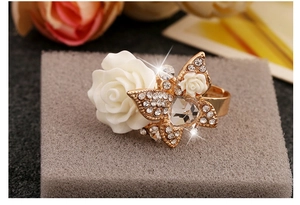Detailed close-up of a white resin rose and crystal butterfly on an open gold ring