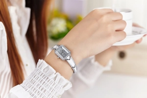 Close-up of a silver rectangular quartz watch with rhinestone accents on a model wrist