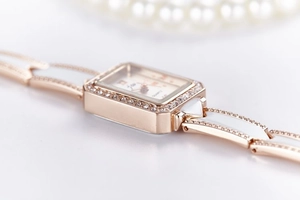 Macro detail of square rose gold quartz watch featuring diamond accents and white dial