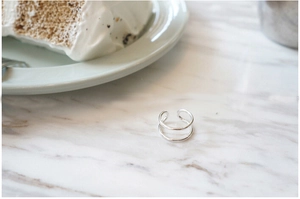 Detail of minimalist S925 sterling silver double-line open ring on marble background