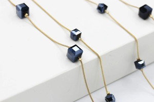 Detalle de un collar largo con cadenas de serpiente doradas y cubos de cristal azul marino
