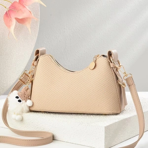 Sac bandoulière tissé beige élégant avec chaîne dorée et breloque ours sur un piédestal