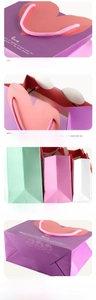 Detail of heart-shaped flap gift bags with pink woven handles and love quote print