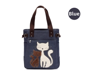 Detail of blue canvas tote bag featuring fuzzy cat patches and brown handles