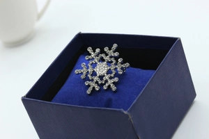 Macro shot of silver snowflake brooch with sparkling rhinestones in a blue jewelry gift box