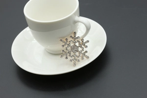 Macro detail of snowflake brooch featuring shimmering rhinestones on a white ceramic cup