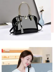 Detail of black patent leather Boston bag with golden braided handles and metal hardware