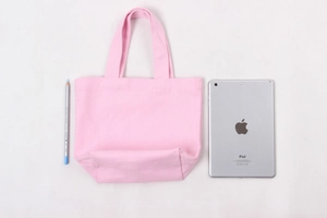 Pink canvas lunch tote bag shown next to an iPad for size comparison on a textured background