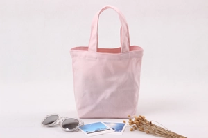 Pink canvas lunch bag shown with travel accessories and dried flowers on white background