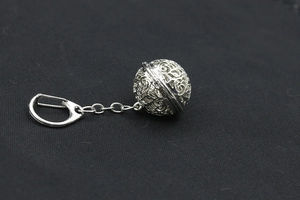 Macro shot of silver hollow spherical pendant and metal chain on black fabric