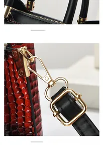 Detailed view of red crocodile-patterned leather bag with black handle and gold buckle