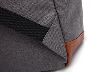 Detail of grey canvas backpack with black strap and brown faux leather corner reinforcement