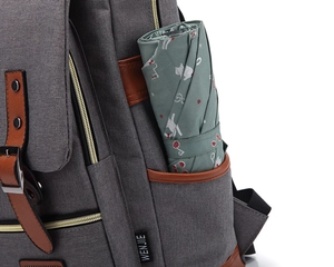 Detail view of grey canvas backpack side pocket with a folded green patterned umbrella