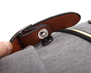 Close-up of gray canvas backpack featuring brown faux leather magnetic buckle closure