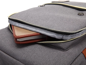 Detail of grey canvas backpack pocket with brown leather trim and metallic zipper
