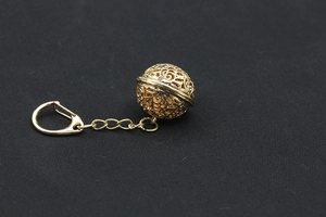 Detail of a hollow golden filigree sphere keychain with a polished metal link and swivel clasp
