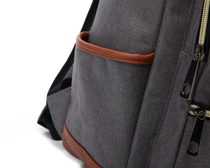 Detail view of grey canvas backpack with brown leather trim and metal zippers