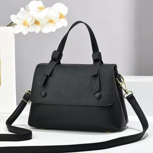 Detail of black pebbled leather crossbody bag with dual buckles and golden hardware
