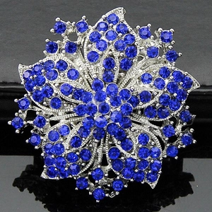 Macro detail of silver floral brooch with dark blue rhinestones on black reflective base