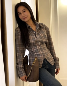 Detailed view of gray and brown plaid long-sleeved shirt styled with a gold chain leather bag