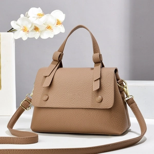 Brown lychee leather saddle bag with top knot handle and gold hardware on minimalist pedestal