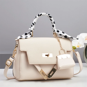 Detail of cream crossbody bag with woven texture flap, golden lock, and polka dot scarf