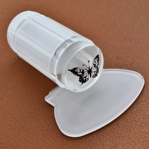 Clear silicone nail stamper with butterfly pattern and white scraper on brown leather surface