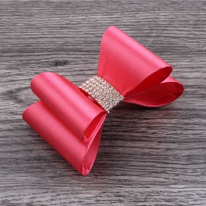 Detail of rose red satin bow hair clip with sparkling rhinestone center on wood background
