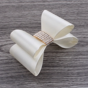 Close-up of cream satin bow hair clip with sparkling rhinestones on wood background