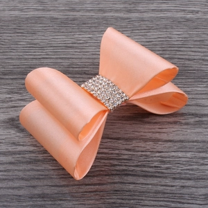 Detail of handmade light orange satin bow clip with elegant five-row rhinestone center