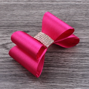 Close-up of rose red satin bow hair clip with sparkling rhinestone center on wood background