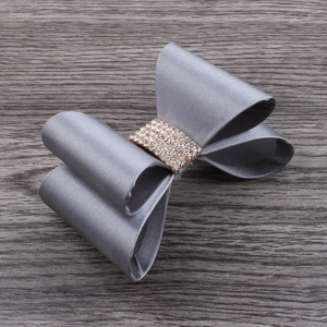 Close-up of grey satin bow hair clip with sparkling silver rhinestone center on wood