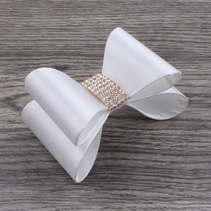 Detail of white satin bow hair clip with sparkling rhinestone centerpiece on wood