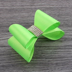 Detail of neon green satin bow hair clip with sparkling silver rhinestones on a wooden surface