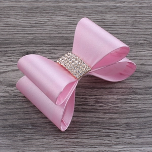 Close-up of pink satin hair clip with sparkling white rhinestones on dark wood